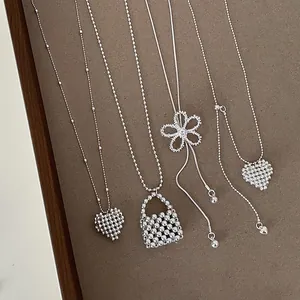 Macro detail of elegant silver beaded necklaces featuring heart and hollow flower pendants.