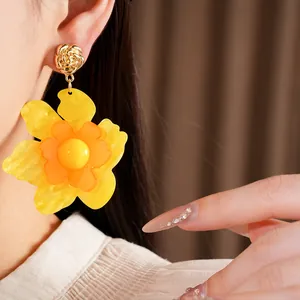 Close-up showing the intricate texture of the yellow resin flower earrings on a model.