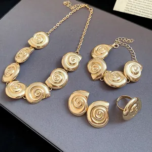 Gold shell jewelry set with necklace, bracelet, earrings, and ring on grey background