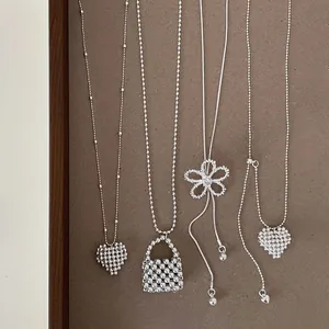 Macro detail view of silver minimalist zircon flower and woven heart necklaces on display.