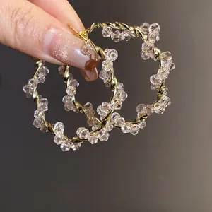 Elegant crystal beaded twisted gold hoop earrings macro view held by a manicured hand