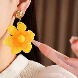 Close-up of large yellow resin flower earrings with gold rose stud and silver needle.