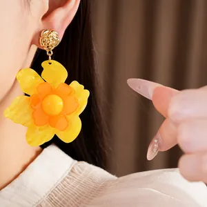 Detail view of vibrant yellow resin flower earrings worn on a model's ear profile