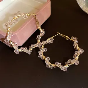Detailed view of large gold twisted hoop earrings featuring clear faceted crystal beads