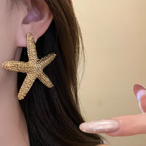 Close-up view of a large textured gold starfish earring on an ear with a manicured hand