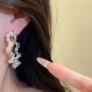 Close-up detail of twisted gold hoop earrings with clear faceted crystal beads on ear