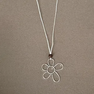 Detailed view of a minimalist hollow flower pendant on a white cord necklace