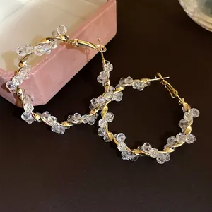 Detailed view of twisted gold-tone hoop earrings with sparkling clear crystal beads.