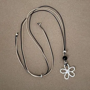 Detail of hollow flower pendant with zircon center on dual-tone cord necklace.