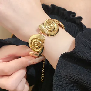 Close-up of vintage gold metal conch bracelet on wrist with elegant black fabric background