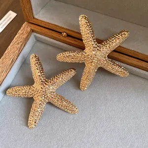 Close-up of golden textured starfish stud earrings with steel pins in a jewelry box