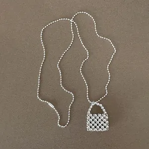 Detailed shot of a minimalist silver ball chain necklace featuring a unique beaded bag pendant