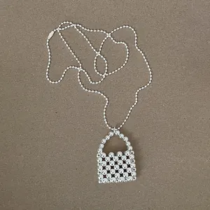 Detail view of silver beaded necklace with unique handbag pendant on brown background.