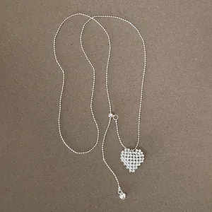 Detail of silver beaded lariat necklace with zircon heart pendant on neutral background