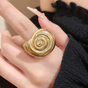 Close-up view of a vintage gold-toned spiral seashell ring worn on a hand with black sleeve