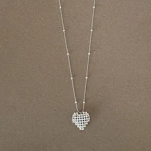 Detailed view of a silver heart-shaped bead pendant necklace on a textured background.