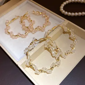 Detail view of twisted gold-toned hoop earrings with clear and pink beads in a box.