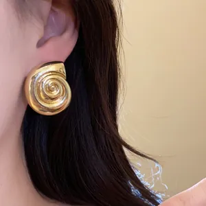 Detailed shot of a vintage golden seashell spiral stud earring worn for elegant style