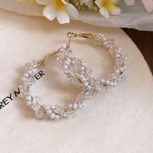 Detailed view of elegant gold-tone hoop earrings decorated with clear crystals and white pearls.