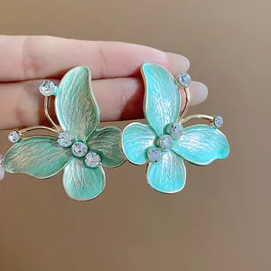 Close-up detail of teal enamel butterfly stud earrings featuring gold edges and clear zircons