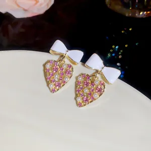 Detalle de los pendientes en forma de corazón con lazos blancos y diamantes de imitación rosas
