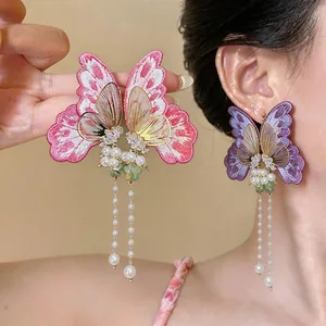 Detailed view of embroidered butterfly earrings with pearls and long tassel fringe.