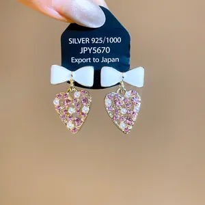 Primer plano de pendientes de corazón con lazos blancos, cristales rosas y perlas