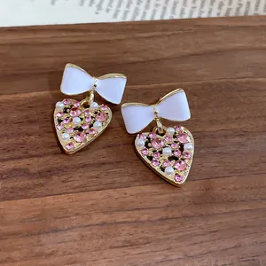 Elegantes pendientes de lazo blanco y corazón de cristal rosa sobre fondo de madera rústica