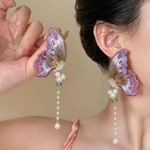 Detailed view of embroidered butterfly earrings with hanging pearls on a model