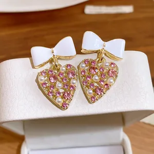 Primer plano detallado de pendientes de corazón con pedrería rosa y un elegante lazo blanco