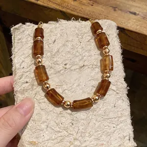 Retro Maillard amber acrylic cylinder and gold bead necklace shown on textured paper