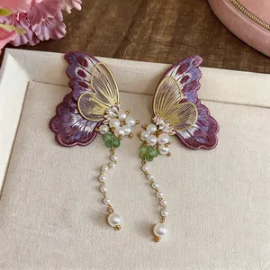 Close-up detail of handcrafted embroidered butterfly earrings with pearls and silver needles
