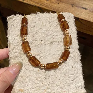 Macro view of Maillard amber acrylic necklace featuring gold bead accents on fiber paper.