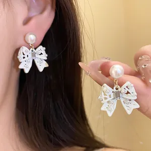 Close-up detail of elegant white bow earrings with pearls and crystals on silver needles