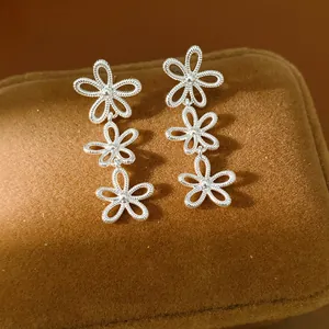 Detailed close-up of silver-toned tiered hollow flower earrings on brown velvet