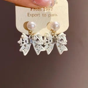 Close-up of elegant white butterfly bow drop earrings featuring delicate pearl studs