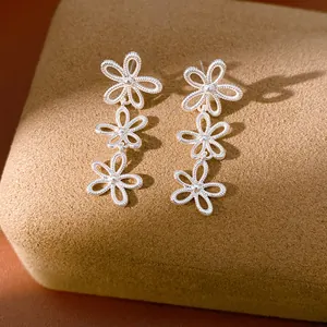 Close-up of elegant silver hollow flower drop earrings on a brown velvet stand.