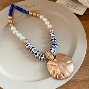 Detail of a vintage ceramic beaded necklace featuring a large textured gold pendant on a plate.