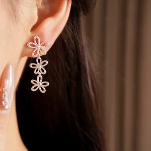 Detail view of silver hollow triple flower drop earrings gracefully worn on model's ear