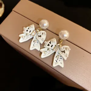 Detailed view of white enamel bow earrings featuring small pearls and a large stud