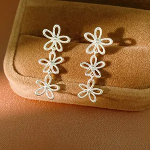 Detailed macro view of silver hollow-out triple flower drop earrings on brown velvet box