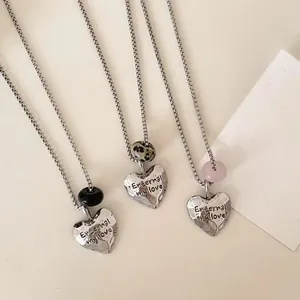 Close-up of silver heart necklaces with various natural stones and engraved love message.