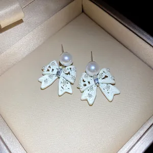 Macro detail view of white bow earrings with pearls and crystal accents in box