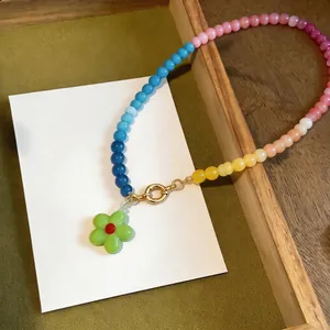Detailed close-up of a colorful gradient glass beaded necklace featuring a green flower pendant