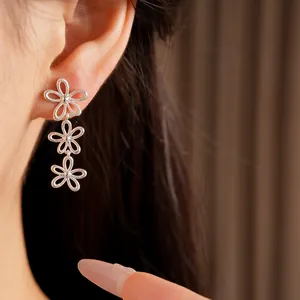 Detail view of minimalist silver hollow triple flower drop earrings worn on the ear