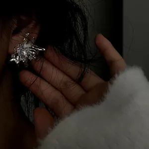 Close-up detail showing a sparkling silver floral zircon stud earring worn on ear with soft textures