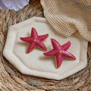 Detail view of pink starfish stud earrings with gold trim and pearl centers on a straw mat