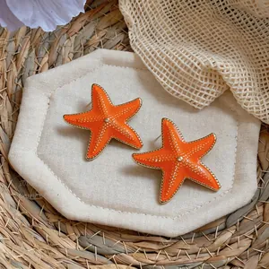 Macro view of vibrant orange enamel starfish earrings perfect for beach vacations.