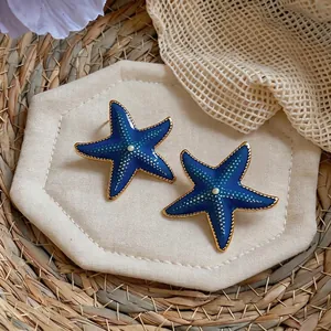 Detailed view of blue enamel starfish earrings with gold trim and pearl center