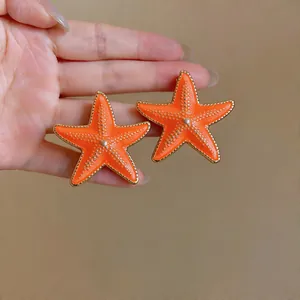 Detailed view of orange starfish enamel earrings with gold-plated edges for beach vacation.